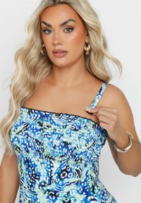 Putketoppi, jossa on sinisen ja vihreän sävyjä sekä abstrakteja kuvioita. Ominaisuuksiin kuuluu ohuet hihnat ja musta reunus. Pehmeää, joustavaa kangasta.