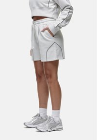 Witte katoenen shorts in een mixmateriaal met een elastische tailleband, zijzakken en contrasterende grijze stiksels. Ggedragen met zilveren sportschoenen.