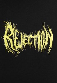 Tessuto nero con testo giallo vibrante e frastagliato che legge "REJECTION". Il design presenta una texture usurata con bordi affilati ed allungati.