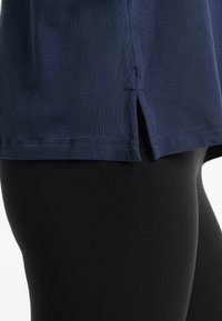 Tengerészkék, rövid ujjú ing, oldalsó hasítékokkal, puha anyagból, fekete, testhez álló leggingszel párosítva. Sima textúra és alapvető design.