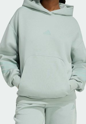 Person iført en lyse mintgrøn Adidas hættetrøje og matchende joggingbukser med diskrete logo- og stribedetaljer på ærmer og bukser.