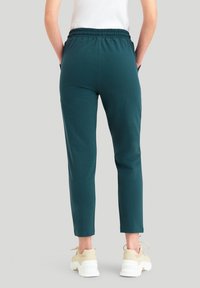 Teal joggingové kalhoty s elastickým pasem, zúženými kotníky a bočními kapsami, spárované s světle zbarvenými robustními teniskami.