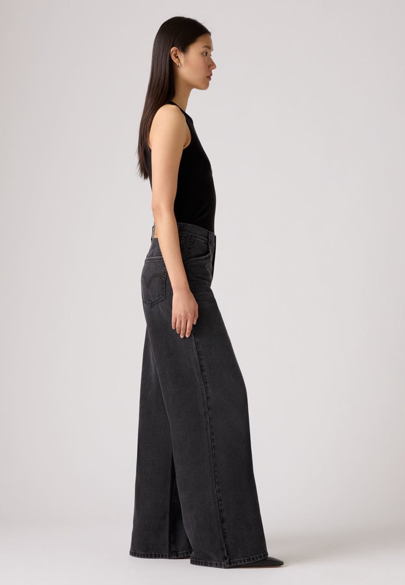 Haut noir sans manches associé à un jean taille haute à jambes larges en denim noir délavé. Le jean comporte des poches classiques et un détail de couture subtil.