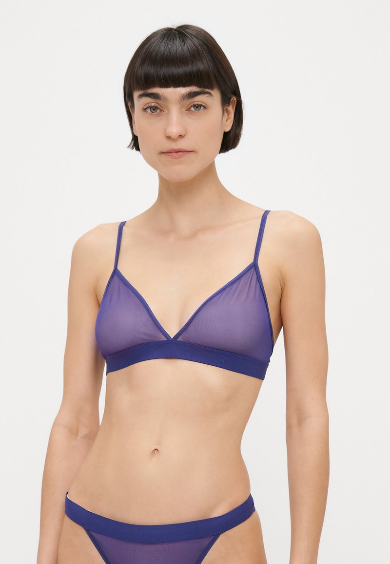Doorzichtige paarse bralette met driehoekige cups, dunne bandjes en een effen donkerpaarse onderband, gecombineerd met bijpassende doorzichtige bikinibroekjes.