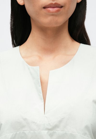 Világoszöld ruha V-nyak kialakítással, puha textúrával és ívelt varrásrészletekkel. Az anyag könnyűnek és simának tűnik.