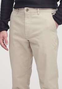 Beige cotton pants with a straight fit. Features a button closure, belt loops, and side pockets. Textured fabric and clean seams are visible.