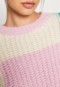 Sweter robiony na drutach z okrągłym, różowym ściągaczem, z kremowym korpusem i różowym paskiem; miękka tekstura z widocznym ściegiem.