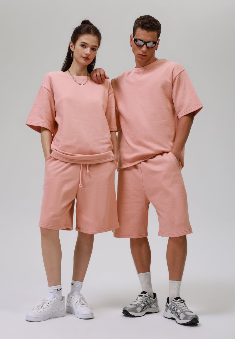 Lichtroze sweatshirt en shorts van zacht materiaal. Kenmerkende relaxed fit, met zichtbare stiksels en details van een trekkoord.