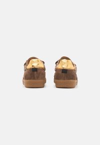 Brown suede sneakers featuring a gold metallic back, textured rubber sole, and stitching accents. Labeled with "Steve Madden."