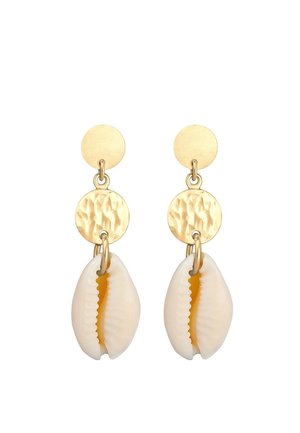 Boucles d'oreilles dorées avec des breloques en disque martelé et des pendentifs en coquillage blanc de cauris pendants en dessous sur un fond blanc.