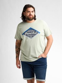 Lichtgroene katoenen t-shirt met een blauwe diamantgrafiek en de tekst "Petrol Ind." Draagt bij donkerdenim shorts met opgerolde zoom.