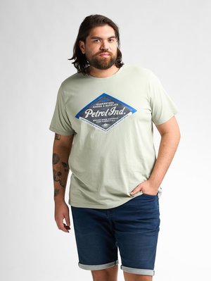Lichtgroene katoenen t-shirt met een blauwe diamantgrafiek en de tekst "Petrol Ind." Draagt bij donkerdenim shorts met opgerolde zoom.