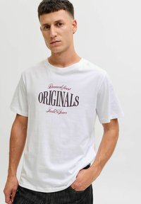 Camiseta blanca de algodón con un atrevido diseño impreso en negro y rojo que dice "Los mejores ORIGINALS de Dinamarca Jack & Jones." Mangas cortas.