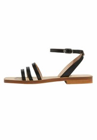 Sandalia de cuero negro con diseño de tres correas, correa de tobillo y hebilla plateada. Suela plana de madera con un acabado suave.