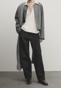 Cardigan en laine gris sur un top crème à col V, associé à un pantalon large noir avec une ceinture nouée, et des chaussures noires brillantes.