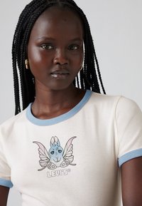 Kremfarget t-skjorte med korte ermer og blå ringer, med et grafisk motiv av sommerfugl og kanin i blå og rosa toner, med "LEVI'S"-tekst.