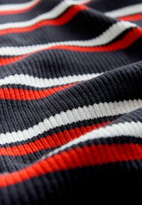 Tissu tricoté avec des rayures horizontales en marine, rouge, blanc et noir. Motif côtelé texturé créant de la profondeur et de l'intérêt visuel.