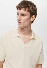 Cream-colored short-sleeve polo shirt with a deep V-neck, textured knit fabric, and contrasting soft collar.