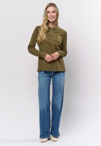 Oliivinvihreä pitkähihaisen poolopaita, jossa on kaulus ja kolme nappia; yhdistetty liehuviin sinisiin farkkuihin ja vaaleisiin kenkiin.