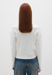 Maglione bianco a maglia lavorata con un orlo a costine e maniche larghe, abbinato a jeans di denim blu a vita alta.
