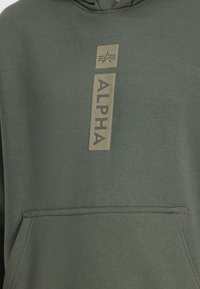 Olivengrøn hoodie lavet af blødt stof, med en frontlomme og et vertikalt, struktureret "ALPHA" logo i lys beige.