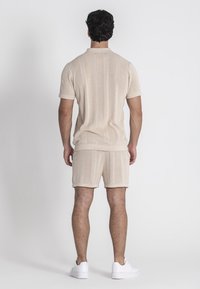 Beige gebreid polo- en shortset met een gestructureerd patroon en verticale strepen. Afgewerkt met ribgebreide zoom en gecombineerd met witte sneakers.