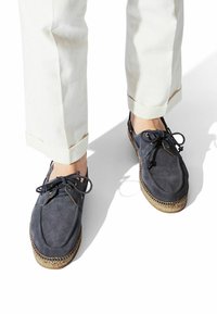 Marineblaue Wildlederschuhe mit Schnürdesign, runden Zehen und gewebtem Jutebesatz an den Sohlen. Kombiniert mit hellen, hochgekrempelten Hosen.