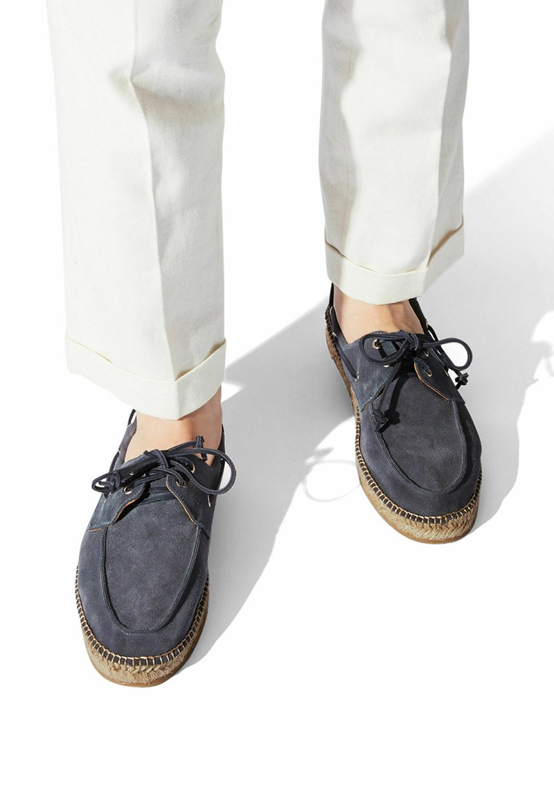 Marineblaue Wildlederschuhe mit Schnürdesign, runden Zehen und gewebtem Jutebesatz an den Sohlen. Kombiniert mit hellen, hochgekrempelten Hosen.
