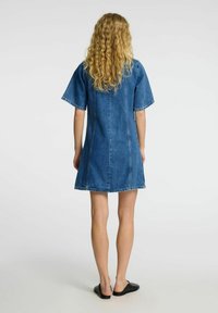 Dongerikjole med korte ermer, lys blå farge, rett snitt og synlige sømdetaljer. Brukt med svarte slip-on sko.