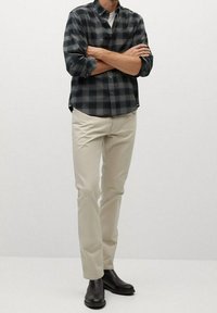 Chemise à carreaux noirs et gris à boutons, chinos crème et bottines en cuir noir. La chemise comporte un col et des manches retroussées.