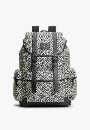 Sac à dos avec motif géométrique beige et bleu foncé, poches avant et latérales, bretelles en cuir noir avec boucles, et écusson logo sur le rabat.