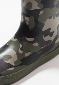 Camouflage rubberschoen in zwart, groen en bruin. Glad afwerking met een gestructureerde groene zool. Enkellange uitvoering met een ronde teen.