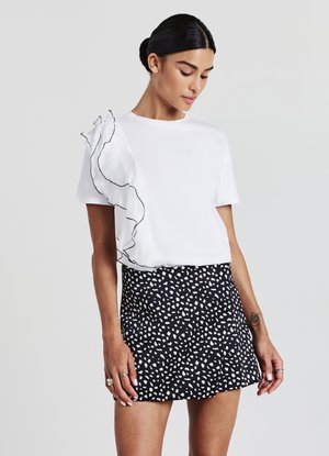 T-shirt blanc avec des accents froncés noirs sur une épaule, associé à une mini jupe noire présentant un motif de points abstraits blancs.