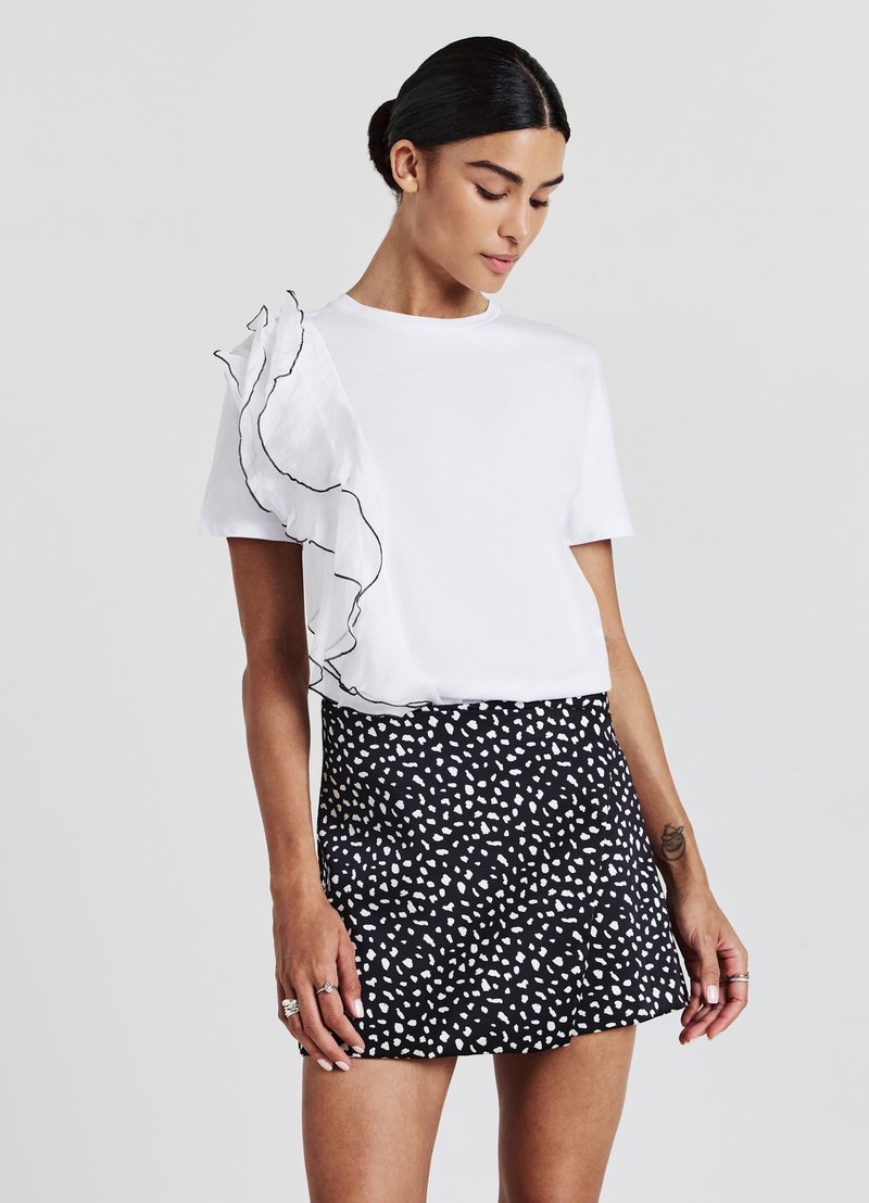 T-shirt bianco con accenti arricciati neri su una spalla, abbinato a una mini gonna nera con un motivo a punti astratti bianchi.
