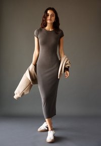 Grau eng anliegendes Kleid mit kurzen Ärmeln, knielang, kombiniert mit einer beigen übergroßen Jacke und weißen Sneakers mit braunen Akzenten.