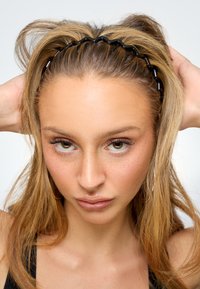 Zwarte golvende haarband ligt op middellang blond haar en benadrukt de gladde textuur en natuurlijke glans tegen een effen achtergrond.