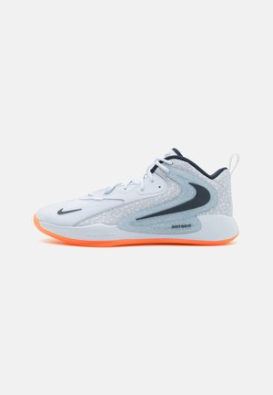 Scarpa sportiva con una tomaia in mesh bianco, accenti grigi e una suola in gomma arancione. Presenta un grande logo a swoosh e il marchio "JUST DO IT".