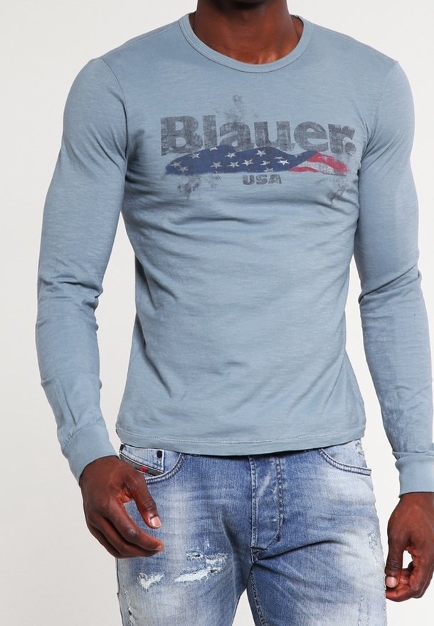 T-shirt à manches longues bleu clair avec un logo graphique délavé, présentant un drapeau américain stylisé et du texte. Tissu doux et coupe ajustée.