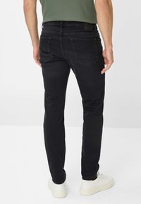 Schwarze Jeans aus Denim mit schmalem Schnitt, ausgestattet mit Gesäßtaschen und einer glatten Textur, kombiniert mit weißen Turnschuhen.