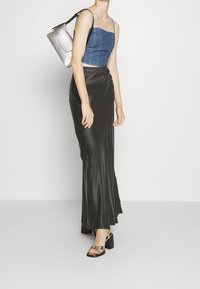 Denimistä valmistettu lyhyt yläosa, tumma satiinihame ja hopeinen käsilaukku. Jalkineissa on kuvioitu design ja paksut korot.