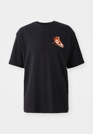 Fekete pamut póló rövid ujjakkal, bal mellkasán egy narancssárga és fehér sneaker grafika található. Tiszta dizájn.