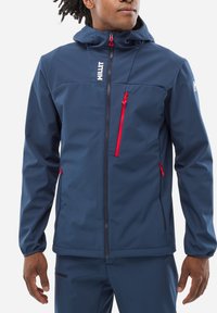 Veste imperméable bleu marine avec capuche, dotée d'accents de fermeture éclair rouge, d'une taille ajustable et d'une poche zippée à l'avant. Texture lisse.