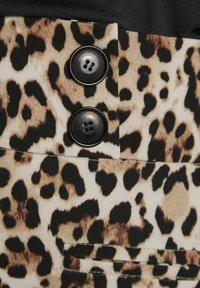 Leopardenmusterstoff mit schwarzen und beigen Flecken; verfügt über zwei schwarze Knöpfe und eine horizontale Naht für das Taschen-Detail.