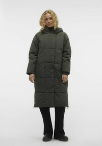 Abrigo acolchado largo de color verde oscuro con capucha, que presenta un patrón geométrico acolchado, cremalleras laterales y puños acanalados, usado sobre pantalones negros.