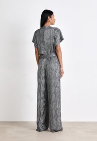 Grå tekstureret jumpsuit med korte ærmer, tætsiddende talje og løse brede ben. Har en bindedetalje bagpå og et lodret stribemønster.