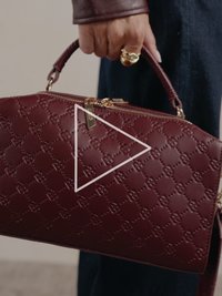 Butelkowoczerwona skórzana torebka z tłoczonym wzorem, podwójnymi uchwytami, złotymi detalami, zamkiem błyskawicznym i odpinanym paskiem.