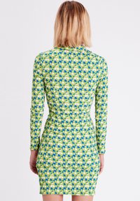 Robe ajustée à manches longues en tissu à motifs verts, bleus et blancs. Elle présente des designs géométriques et une taille cintrée.