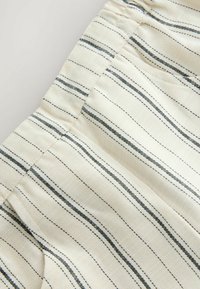 Tissu crème avec de fines rayures bleu marine. Il présente une taille froncée. La texture semble lisse avec des détails tissés.