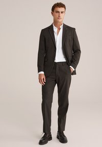 Donkergrijs pak met een op maat gemaakt jasje en bijpassende broek. Witte overhemd eronder en bruine leren schoenen. Gladde textuur, moderne snit.