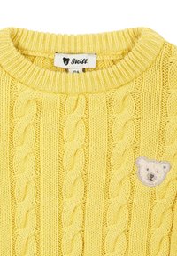 Maglione giallo lavorato a maglia con motivo a treccia e un'applique a forma di orso. Presenta un collo a costine e un'etichetta del marchio sul colletto.